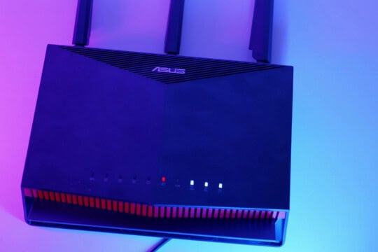 An Asus RT-AX86U Pro router on a pink and blue background.